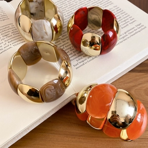 Detail of stacked acrylic marble resin bracelets with gold metal links on a book