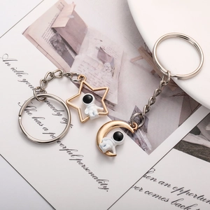 Star and moon astronaut couple keychain in golden finish on a romantic postcard background