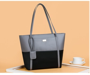 Detail of gray and black patchwork faux leather tote bag with elegant metal plate accent