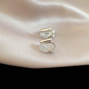 Close-up of silver U-shaped clip-on earrings with clear anti-pain resin pads on satin