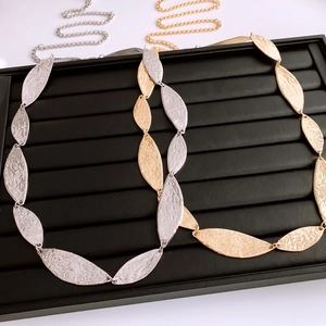 Macro detail of leaf-shaped metal chain links with hammered texture in gold and silver