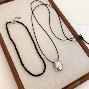 Detail of a silver pebble pendant on a black cord next to a black beaded necklace