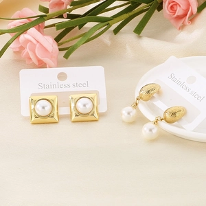 Macro view of gold-plated stainless steel earrings with pearl insets on silk fabric