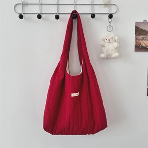 Close-up of a large red quilted fabric tote bag hanging against a white wall