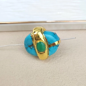 Detail of irregular blue gemstone and green bead with golden crisscross metal wrap