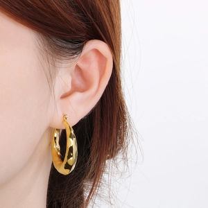 Close-up of hammered 18K gold-plated U-shape earrings worn by a model in white background