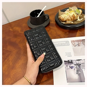 Close-up of a long black quilted leather wallet on a wooden table with lifestyle props