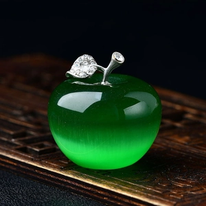 Macro detail of a green cat eye stone apple ornament with crystal leaves on a wooden surface