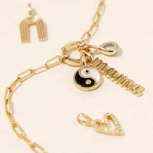 Detailed close-up of golden necklace with Yin Yang, heart, and mama letter charms
