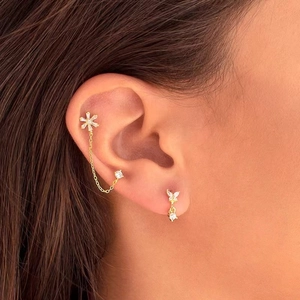 Close-up of gold butterfly and snowflake stud earrings set with white zircons on ear