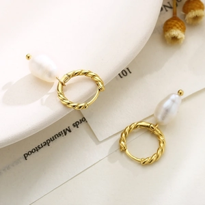Detail of golden twist hoop earrings with elegant baroque pearl pendants on white plate