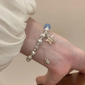 Macro shot of silver beaded bracelet with star and flower charms on a model's wrist