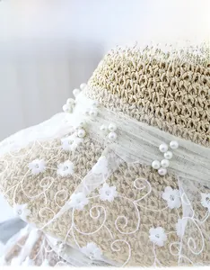 Macro detail of beige straw hat with delicate white lace embroidery and pearl accents