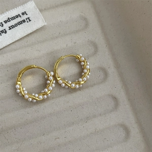 Close-up of French-style gold pearl hoop earrings on a minimalist beige tray