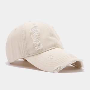 Détails d'une casquette beige en coton vieilli avec effets d'usure et déchirures latérales