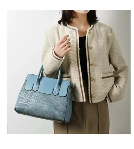 Detail of light blue handbag showing croc-embossed texture and protective metal base studs