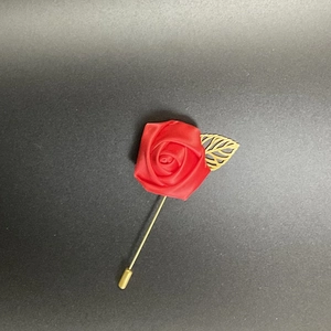 Close-up of a red satin rose lapel pin with a gold hollowed leaf on a long needle