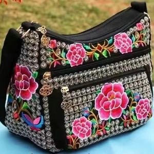 Ethnic floral embroidered canvas shoulder bag with multi-zipper compartments on grass