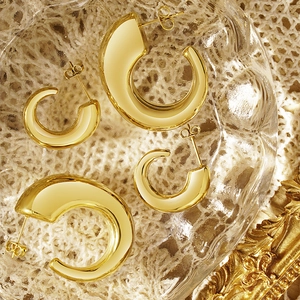 Polished gold C-shaped chunky hoop earrings set displayed on a vintage glass tray
