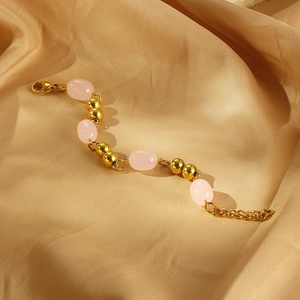 Detailed view of gold bead and pink resin bracelet on elegant champagne satin fabric