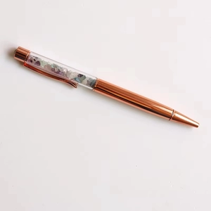 Detail of rose gold ballpoint pen showing transparent barrel filled with colorful crystals