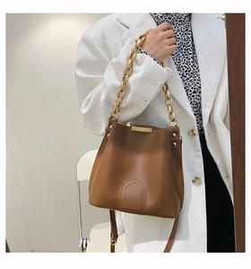 Detail view of brown leather bucket bag with chunky gold chain strap and stitching