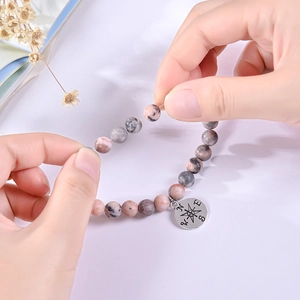 Elastic stretch test of natural stone bead bracelet featuring a compass pendant detail