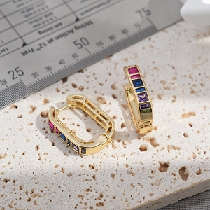 Close-up of luxury brass earrings with colorful rectangular zircons on stone surface
