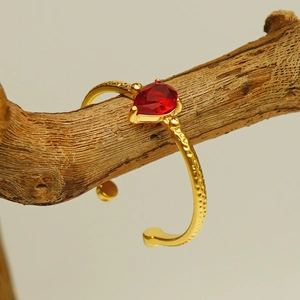 Goldener Hammerschlag-Ring mit rotem Zirkon-Tropfenstein auf rustikalem Ast
