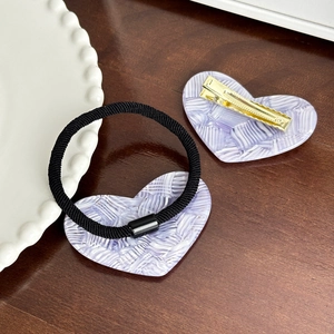 Elegant purple heart hair tie and gold clip set on a wooden surface with a ceramic plate