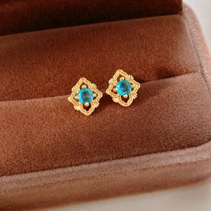 Close-up of vintage gold hollow earrings with bright blue sapphire-style zircon stones