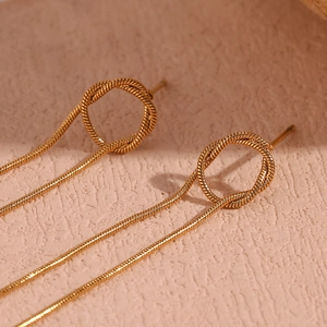 Macro shot of gold-plated twisted ring and long snake chain tassel earrings detail