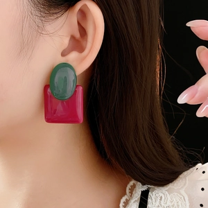 Close-up of geometric resin stud earrings featuring green oval and red square shapes