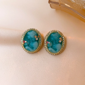 Vintage cameo earrings with green oval portraits and colorful crystals on beige fabric