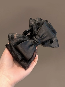Detail of black satin and polka dot organza layered bow hair claw clip held in hand