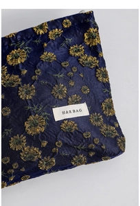 Detailed close-up of dark blue jacquard fabric with golden daisy embroidery and label