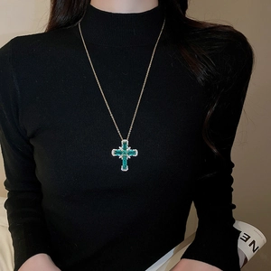 Détail du pendentif croix avec zircon vert sur collier doré porté par un mannequin