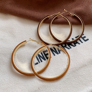 Brown flocked geometric hoop earrings with gold metal core on beige fabric background