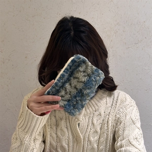 Detail of plush fuzzy blue and grey storage pouch held by model in knit sweater