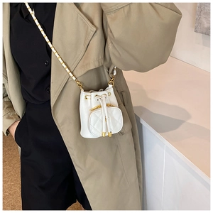 Mini white bucket bag with camellia drawstring and gold chain worn with a trench coat