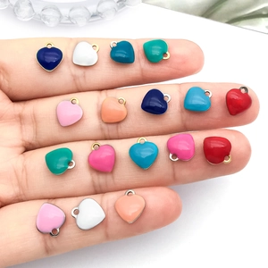 Colorful enamel heart pendants for DIY jewelry shown on a finger for scale and size