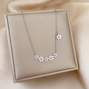 Detail view of dainty white daisy charms on a titanium steel necklace in a beige jewelry box