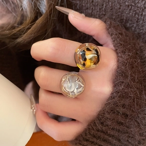 Close-up of tortoise shell and cream resin chunky rings worn with a brown sweater