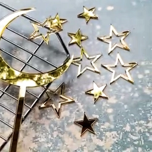 Close-up of gold mirror acrylic moon and star cake toppers on a grey textured surface