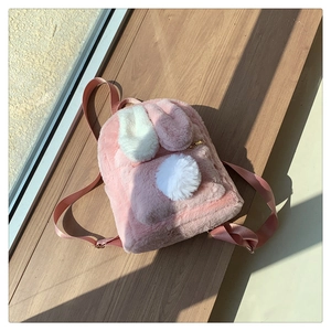 Detail of pink plush bunny backpack with white ears on a wooden windowsill in natural light