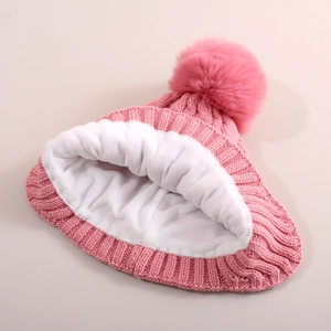 Detail of pink cable knit baby hat featuring thick white fleece lining and soft faux fur pom
