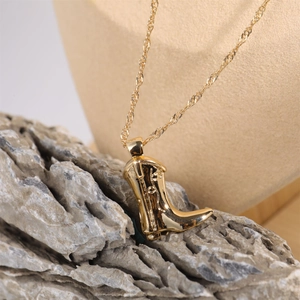 Golden cowboy boot pendant with rope chain necklace displayed on a textured stone