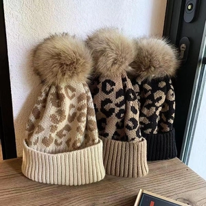 Stylish leopard print knit hats with large fur pom-poms in beige, brown, and black
