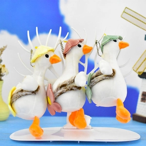Trois mignons porte-clés oies en peluche avec chapeaux colorés sur un support blanc