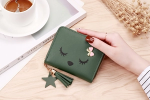 Close-up of green tassel coin purse with cartoon face and pink bow on a wooden table